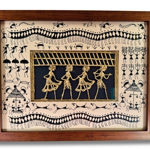 May include: A framed artwork depicting a traditional Indian folk art style with black and white figures and a central gold-coloured metal panel featuring four figures dancing under a striped canopy.