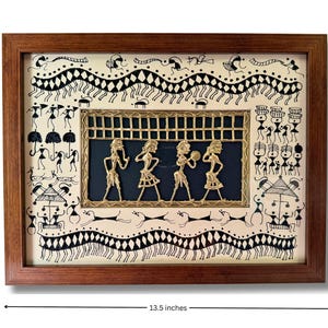 May include: A framed artwork depicting a traditional Indian folk art style with black and white line drawings of people and animals. The artwork features a central panel with four figures made of gold metal, set against a dark blue background. The frame is made of dark wood and measures 13.5 inches by 10.5 inches.