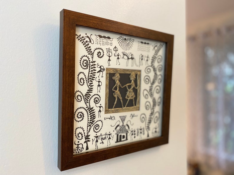 May include: A framed artwork with a white background and black line drawings of people, animals, and plants. The artwork is surrounded by a dark brown frame.