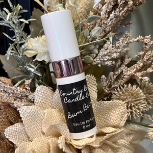 Puede incluir: Botella blanca con una etiqueta negra que dice "Country Lane Candle Co. Bum Bum" y "Eau De Parfum 8 ml".