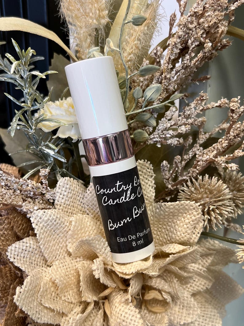 Puede incluir: Botella blanca con una etiqueta negra que dice "Country Lane Candle Co. Bum Bum" y "Eau De Parfum 8 ml".
