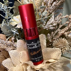 Puede incluir: Una botella roja de perfume Volcano de Country Road Candle Co. La botella est&aacute; etiquetada con el nombre de la empresa, el nombre del perfume y "Eau De Parfum 8 ml".