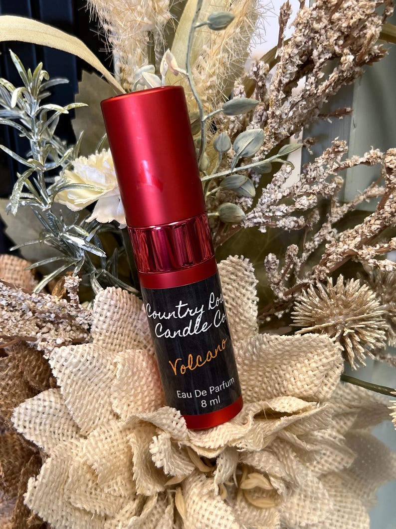 Puede incluir: Una botella roja de perfume Volcano de Country Road Candle Co. La botella est&aacute; etiquetada con el nombre de la empresa, el nombre del perfume y "Eau De Parfum 8 ml".
