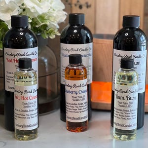 May include: Three large black bottles and three smaller clear bottles of Country Road Candle Co. fragrance oils. The labels list scents including Red Hot Cinnamon, Blueberry Cheesecake, and Bum Bum, along with flash points and vanillin percentages.