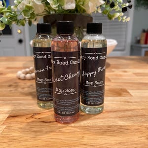 May include: Three bottles of Country Road Candle Mop Soap, each with a black label and a different colored liquid. The bottles are labeled "Lemon Fr," "Sweet Cherry," and "Happy Pine." Each bottle contains 4 fl oz (118 mL).