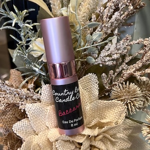Puede incluir: Una botella de perfume rosa y plateada con una etiqueta negra que dice "Country Love Candle Co.  Baccarat Eau De Parfum 8 ml".