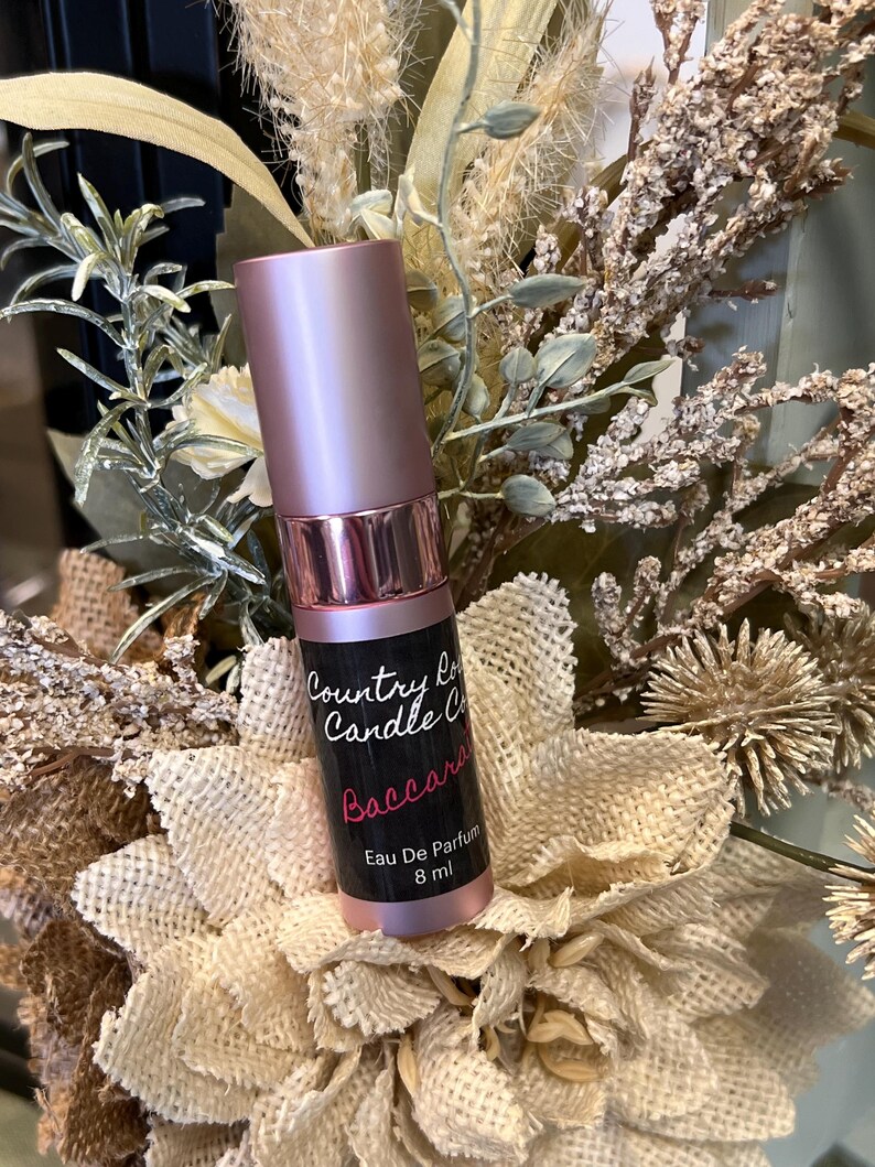 Puede incluir: Una botella de perfume rosa y plateada con una etiqueta negra que dice "Country Love Candle Co.  Baccarat Eau De Parfum 8 ml".