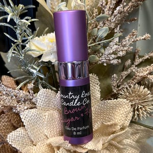 Puede incluir: Una botella morada de perfume con aroma a az&uacute;car moreno y higo de Country Road Candle Co. La botella es de 8 ml y dice "Eau De Parfum" en la etiqueta.