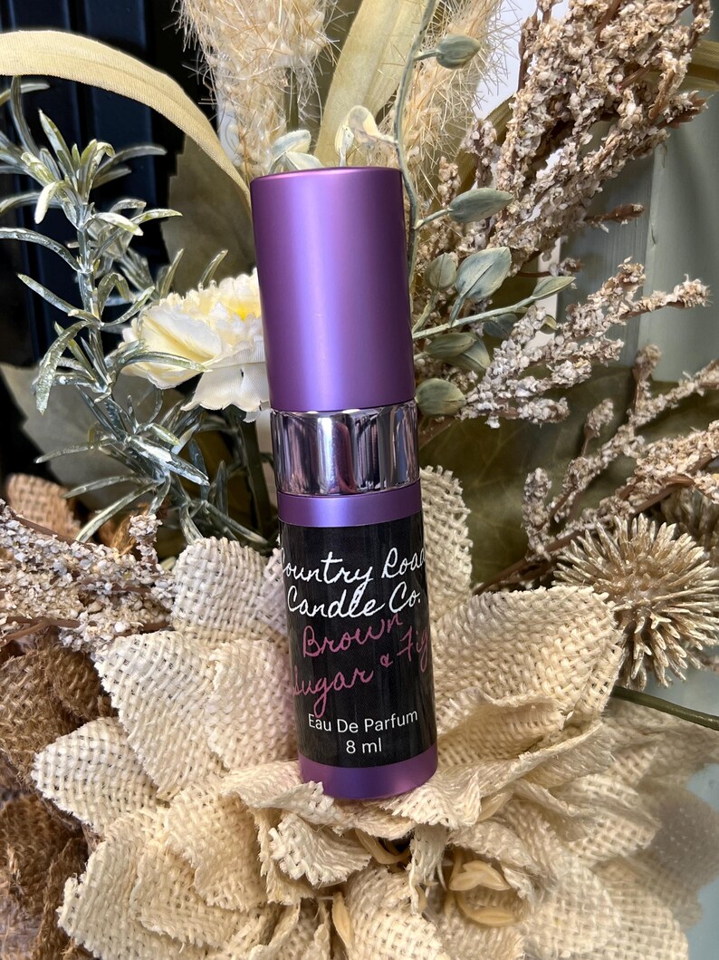 Puede incluir: Una botella morada de perfume con aroma a az&uacute;car moreno y higo de Country Road Candle Co. La botella es de 8 ml y dice "Eau De Parfum" en la etiqueta.