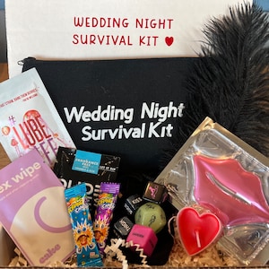 Könnte beinhalten: Eine schwarze Box mit der Aufschrift "Wedding Night Survival Kit" auf dem Deckel. Die Box enthält verschiedene Artikel, darunter eine schwarze Tasche, eine rosa Lippenmaske, eine herzförmige Kerze, eine Federboa und eine Packung Süßigkeiten.