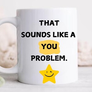 May include: White ceramic mug with black text that reads "That sounds like a you problem." A yellow star with a smiley face is below the text.