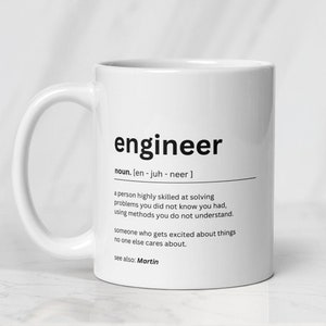 May include: White ceramic mug with a black design that defines the word "engineer" and its pronunciation. The definition reads: "a person highly skilled at solving problems you did not know you had, using methods you do not understand. someone who gets excited about things no one else cares about. see also: Martin."