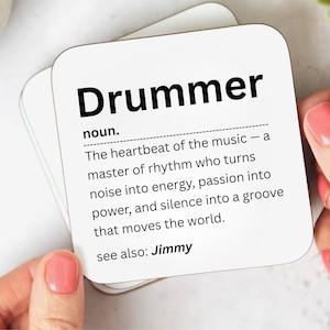 May include: Square white coaster featuring the word "Drummer" in black, bold font. The coaster defines "Drummer" as the heartbeat of music. The text also includes "see also: Jimmy".