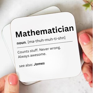 May include: Square white coaster with the word "Mathematician" and its definition printed in black. The definition includes the pronunciation, "Counts stuff. Never wrong. Always awesome." and "see also: James."