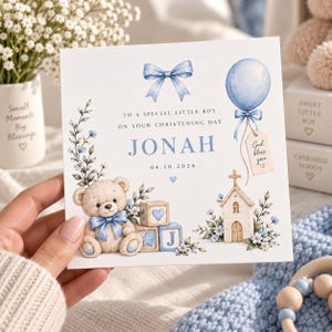 Puede incluir: Una tarjeta de bautizo cuadrada con una ilustración en acuarela de un osito de peluche con un lazo azul, un globo azul con una etiqueta que dice God bless you, una pequeña iglesia y bloques. El texto dice: TO A SPECIAL LITTLE BOY ON YOUR CHRISTENING DAY JONAH 04.10.2026.