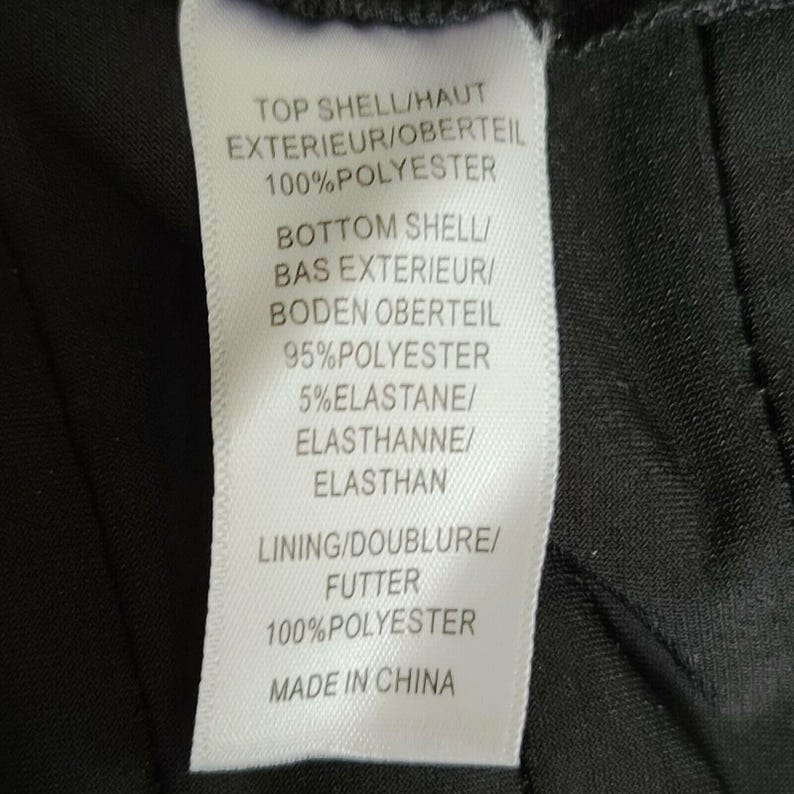 Puede incluir: Una etiqueta de ropa blanca con texto negro. Detalla la composici&oacute;n de la tela, indicando 100% poli&eacute;ster para la capa superior y el forro, y 95% poli&eacute;ster y 5% elastano para la capa inferior. La etiqueta tambi&eacute;n indica "Made in China."