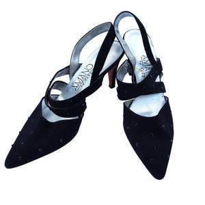 May include: A pair of black slingback heels with pointed toes. The shoes feature multiple straps, small embellishments, and a silver insole with the brand name "AMANO" printed on them. The heels are approximately 3 inches high.