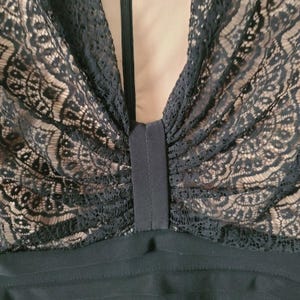 Puede incluir: Primer plano de un corpi&ntilde;o de vestido negro con cuello en V pronunciado. La secci&oacute;n superior presenta un intrincado encaje negro sobre un forro nude. Una banda negra vertical recorre el centro y la parte inferior tiene detalles acanalados horizontales.