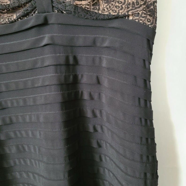 Puede incluir: Vestido negro con corpi&ntilde;o plisado y escote de encaje. El vestido tiene una silueta ajustada y parece estar hecho de una tela fluida. El detalle de encaje a&ntilde;ade un toque de elegancia al dise&ntilde;o general.