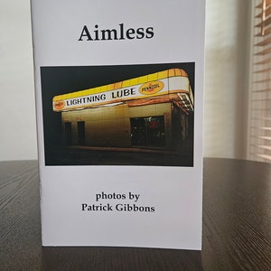 Puede incluir: Un libro blanco con el título "Aimless" impreso en negro. La portada presenta una fotografía de una gasolinera amarilla y negra con las palabras "Lightning Lube" y "Pennzoil" en el toldo. El libro es de Patrick Gibbons.