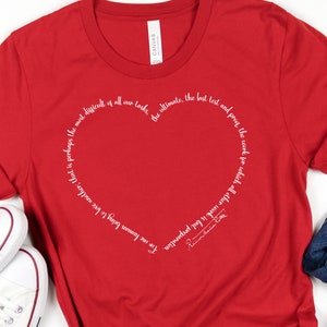 May include: Red t-shirt with a white heart design and a quote around the heart that reads: "For one human being to love another; that is perhaps the most difficult of all our tasks. The ultimate, the last test and proof the work for which all other work is but preparation." -  Rainer Maria Rilke
