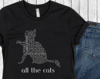 Peut inclure: T-shirt noir avec un design de nuage de mots blanc de races de chats en forme de chat. Le texte en bas du t-shirt est "all the cats".