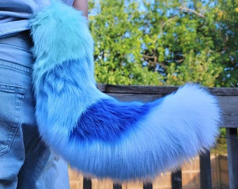 May include: A fluffy blue, teal, and white faux fur tail with a long, flowing design. The tail is attached to a person's waist.