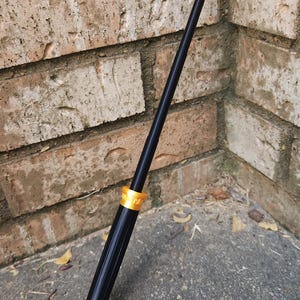 Puede incluir: Una varita negra con detalles dorados. La varita está hecha de madera y tiene un acabado liso y pulido. La varita mide aproximadamente 30 cm de largo y tiene una punta puntiaguda.