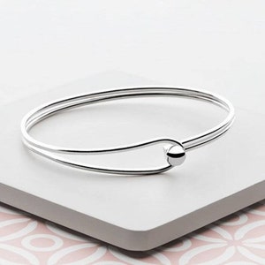 May include: A silver bangle bracelet with a smooth, round bead at the clasp.