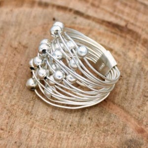 May include: A silver ring with multiple thin bands and small silver beads. The ring is designed to be worn on the knuckle.