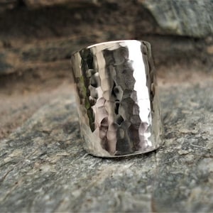 May include: A silver hammered ring with a wide band. The ring is made of metal and has a textured surface.