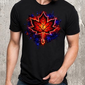 Puede incluir: Una camiseta negra de manga corta con un gráfico central de una hoja de arce. La hoja está representada en tonos vibrantes de rojo, naranja y amarillo, rodeada por un efecto de salpicaduras de pintura azul oscuro y violeta brillante.