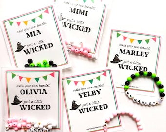 May include: Four colorful cards with the text "make your own bracelet" and a witch's hat graphic. Each card has a different name: Mia, Mimi, Marley, Olivia, and Yelby. The text "just a little wicked" is on each card.  There are also five bags of colorful beads, and two bracelets with the names "Marley" and "Yelby" on them.