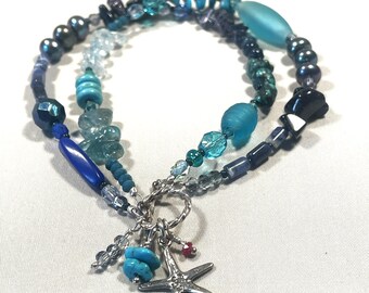 May include: A layered bracelet featuring various blue and turquoise beads, including faceted, round, and irregular shapes. A silver starfish charm and turquoise beads dangle from the bracelet, creating a nautical theme.