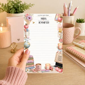 Könnte beinhalten: Ein liniertes Notizblock mit floralem und schulischem Design. Der Notizblock trägt oben den Text "A Little Note From Mrs. Jennifer". Das Design umfasst Äpfel, Bleistifte, Bücher und eine Kaffeetasse.