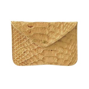 May include: A gold-coloured clutch bag with a textured, reptile-like pattern. The envelope-style flap is secured with a small, round, gold-toned button. The edges are neatly stitched, and the overall design is sleek and stylish.