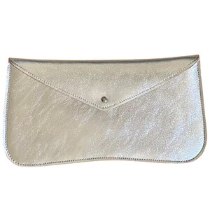 Könnte beinhalten: Eine silberne Metallic-Clutch mit Klappenverschluss und einem einzigen Druckknopf.