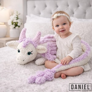 Könnte beinhalten: Ein großes, weiches, gehäkeltes Drachen-Stofftier mit cremefarbenem Körper und hellvioletten Akzenten an Hörnern, Mähne, Flügeln und Schwanz. Der Drache hat dunkle, ausdrucksstarke Augen und einen langen, segmentierten Schwanz, der sich vorne kringelt.