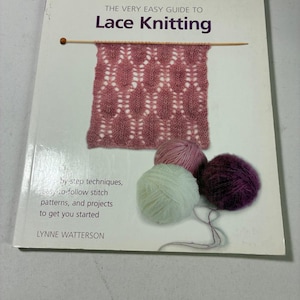 May include: A softcover book titled The Very Easy Guide to Lace Knitting by Lynne Watterson. The cover features a pink lace-knitted swatch on a wooden needle, accompanied by three balls of yarn in light green, pink, and dark purple colours.
