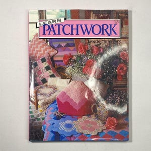 May include: A softcover book titled Learn Patchwork by Lynette-Merlin Syme. The cover features a colourful display of quilted items, including a pink scalloped tea cosy, various patterned patchwork quilts, and a bouquet of red roses in a vase.