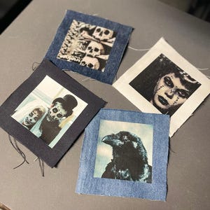 May include: Four fabric patches with different images. One patch features a black and white image of three skulls. Another patch features a black and white image of a woman with dark hair and makeup. The third patch features a black and white image of two people with painted faces. The fourth patch features a black and white image of a raven with a blue background.