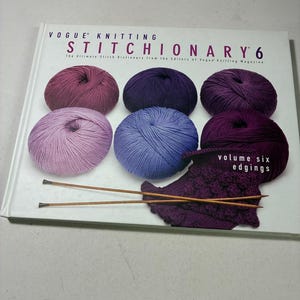 May include: A hardcover book titled Vogue Knitting Stitchionary 6, The Ultimate Stitch Dictionary from the Editors of Vogue Knitting Magazine, volume six edgings. The cover features six yarn balls in purple shades and two wooden knitting needles.