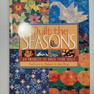 May include: A softcover book titled Quilt the Seasons: 24 Projects to Build Your Skills by Barbara K. Baker & Jeri Boe. The cover features a collage of quilted patterns including flowers, a bird, pumpkins, and landscapes in vibrant colours.