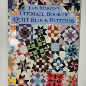 May include: A softcover book titled Judy Martin's Ultimate Book of Quilt Block Patterns. The cover features a collage of various colourful geometric quilt block designs in shades of blue, red, green, yellow, and purple against a white background.