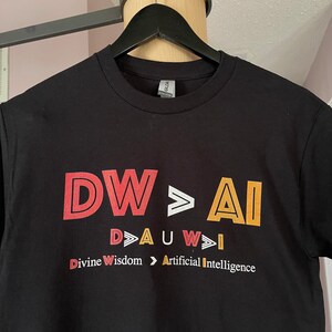 Peut inclure: T-shirt noir avec le texte "DW>AI" en rouge, blanc et jaune. Le texte "D>AUW>I" est en dessous du texte principal en plus petit. Les mots "Divine Wisdom > Artificial Intelligence" sont en dessous du texte plus petit.