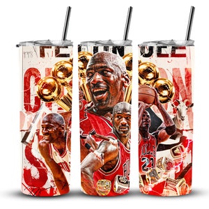 以下が含まれることがあります： バスケットボール選手とチャンピオンシップトロフィーが描かれた、赤、白、黒のデザインのステンレス製タンブラー。タンブラーには蓋とストローが付いています。タンブラーには「The Greatest」という文字が見えます。