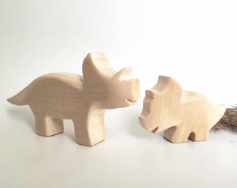May include: Two wooden dinosaur toys, one larger than the other, are carved in the shape of a Triceratops. Both are unpainted and made of light wood.