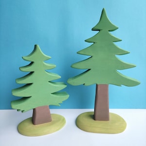 Peut inclure: Deux sapins en bois vert avec des troncs et des bases marrons sur un fond bleu clair. Le plus grand arbre est à droite et le plus petit à gauche.
