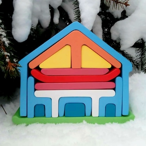 May include: A colorful wooden toy house with a blue roof, yellow, orange, and red walls, and a green base. The house is made of stacked pieces that can be assembled and disassembled.