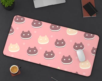 May include: A pink rectangular mouse pad with a repeating pattern of cat-shaped cookies in brown and beige. The pad has a black border and is surrounded by office supplies, including a laptop, mouse, and pens.